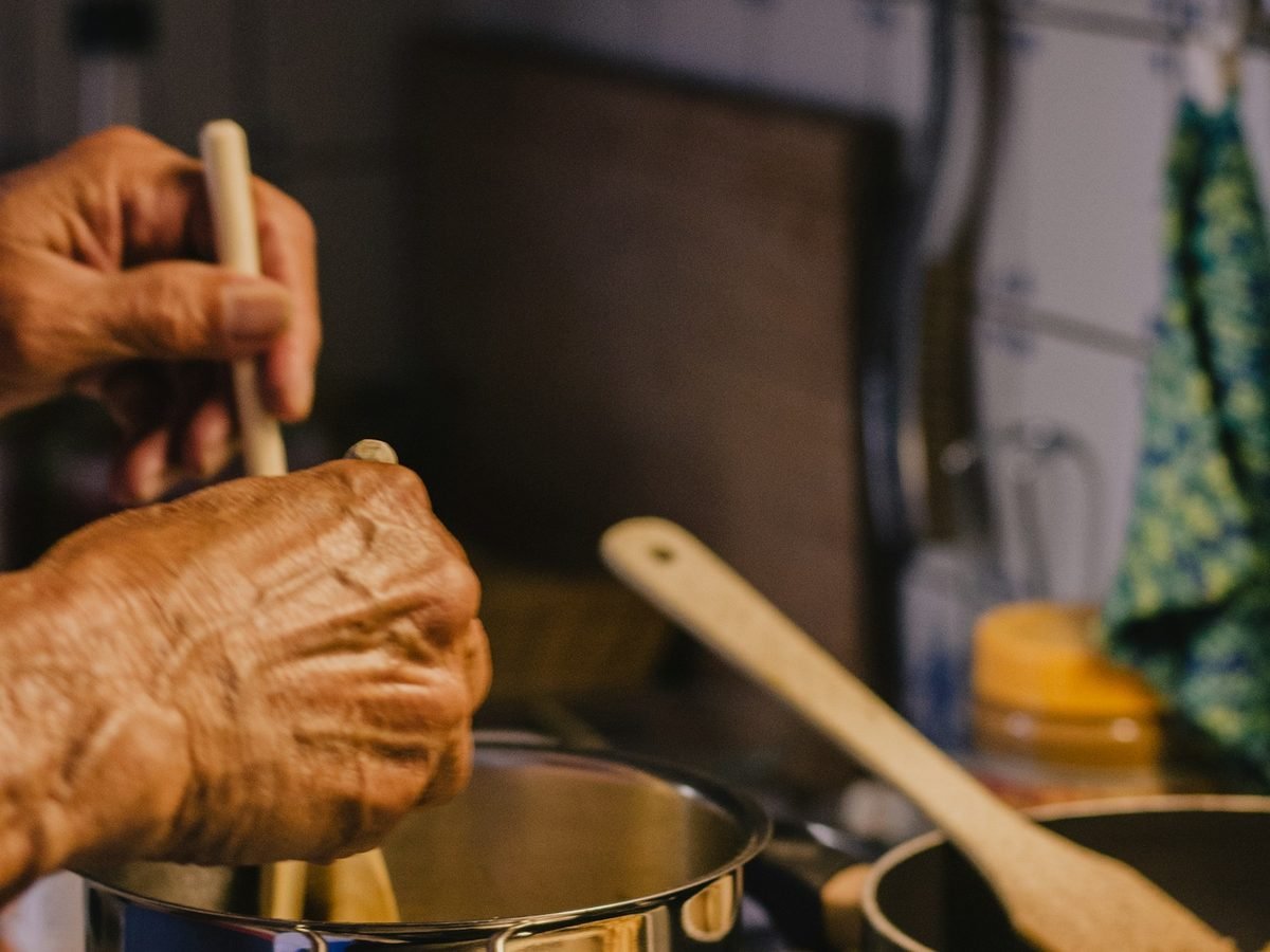 Weathered hands stirring a pot on the stove, cooking a meal from scratch